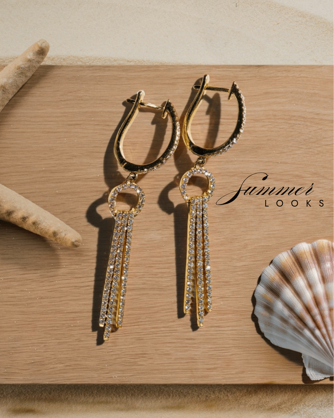 Elegant gold dangle earrings with crystal accents displayed on a wooden surface, styled with starfish and seashells for a summer jewelry look
